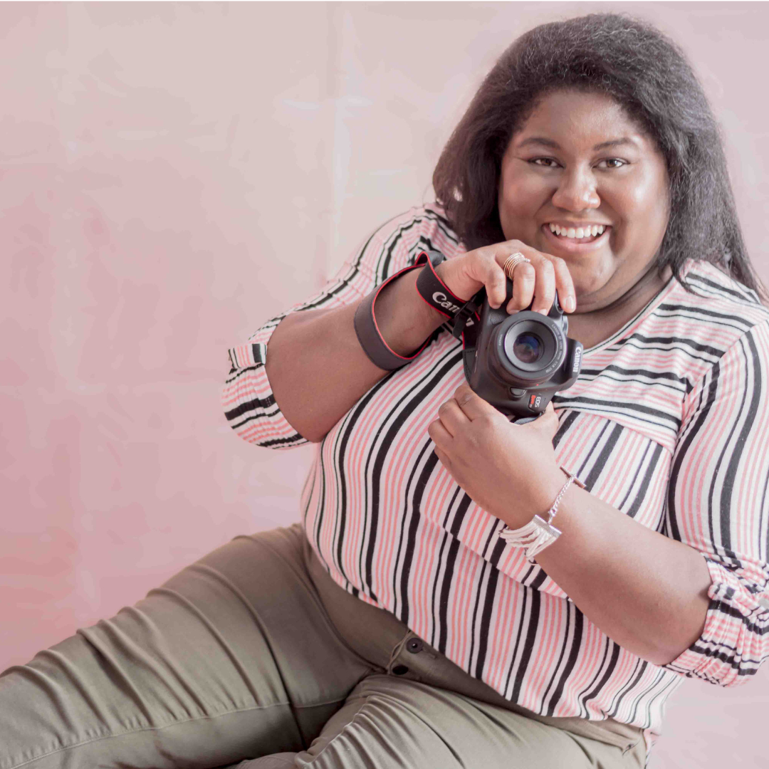 Founder and lead photographer LaDonna Takyi Taylor posed on pink background holding Canon DSLR camera and a big smile. Syracuse, NY Central New York CNY wedding photography. North Country, northern new york portrait photographer