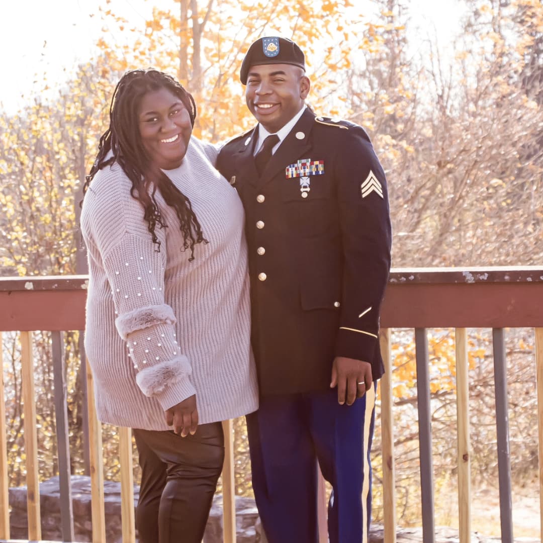 founder LaDonna Takyi Taylor with co-owner and husband, SGT Demetrius Taylor who is dressed in formal U.S. Army uniform. They are embracing each other in a golden, woodsy, outdoor setting on Fort Drum, NY