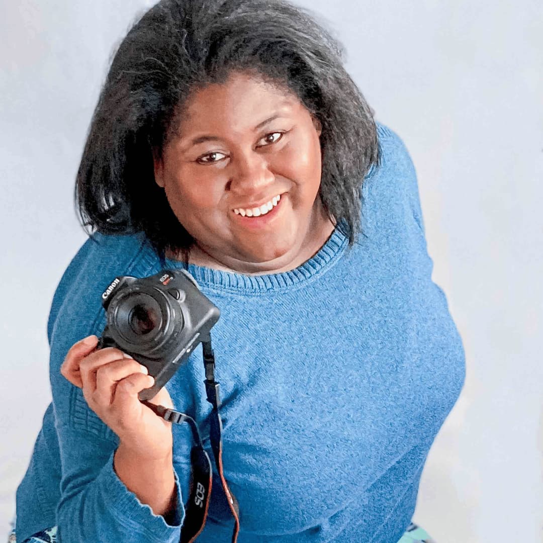 Founder LaDonna Takyi Taylor posing on white backdrop, smiling, holding Canon DSLR camera
