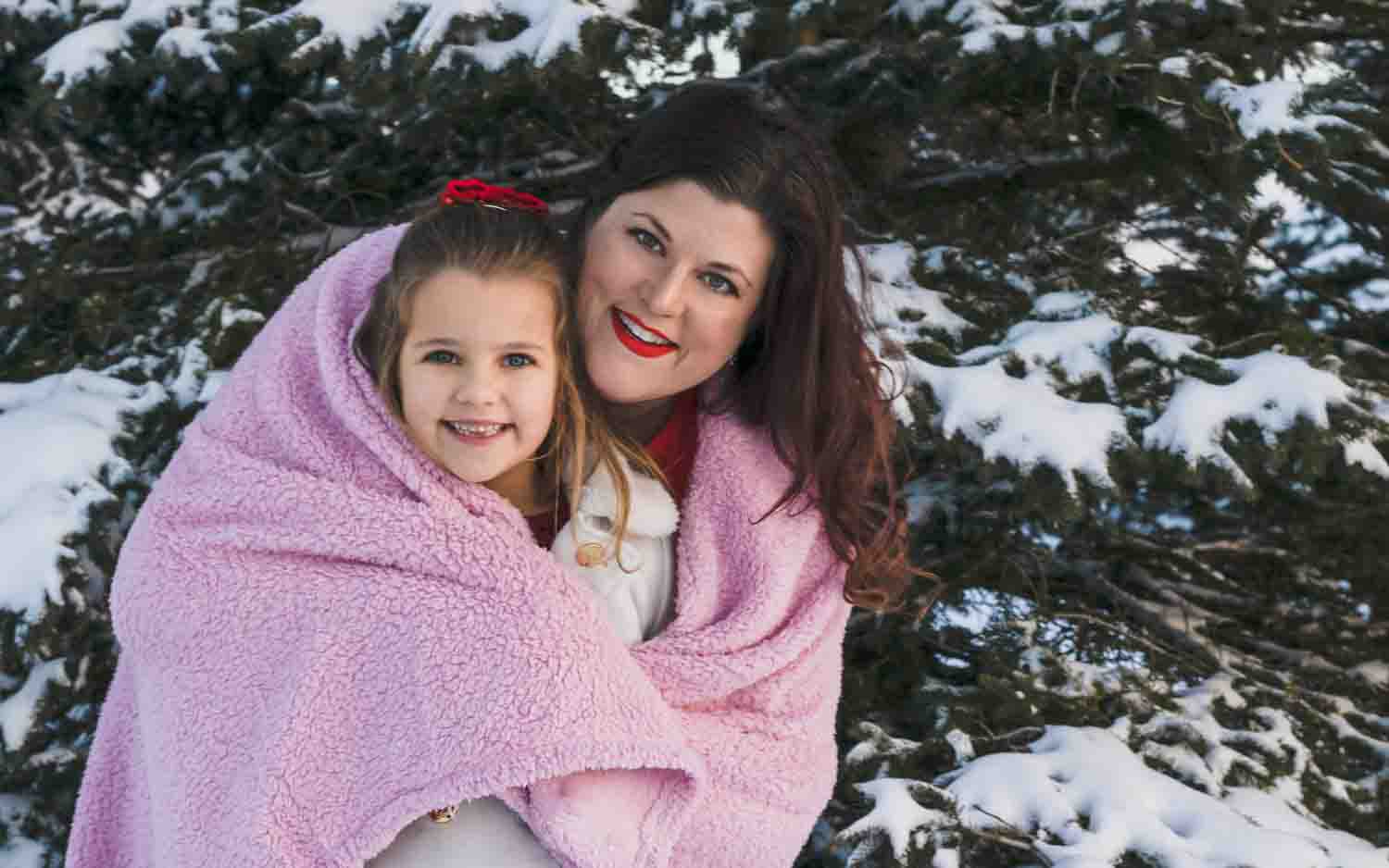 Family portrait - mommy daughter both smiling faces 
 wrapped in pink faux fur throw blanket in front of snow covered pine trees. Military family photography. Fort Drum NY Watertown, NY
