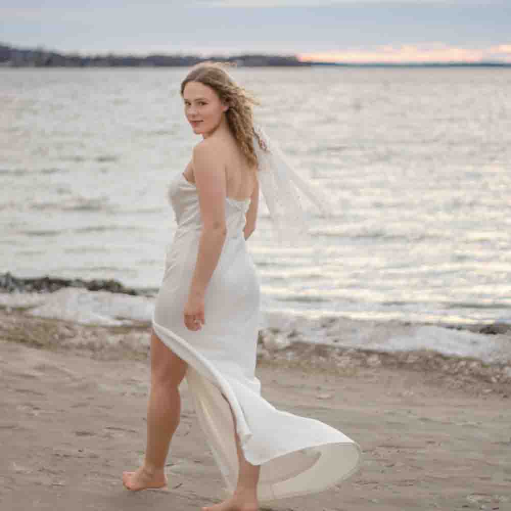 Bridal photography- portrait of a bride walking barefoot on the beach - ocean behind her
white wedding gown, Lake Ontario in the background. bright light and airy photography. Westcott Beach, Alexandria Bay New York