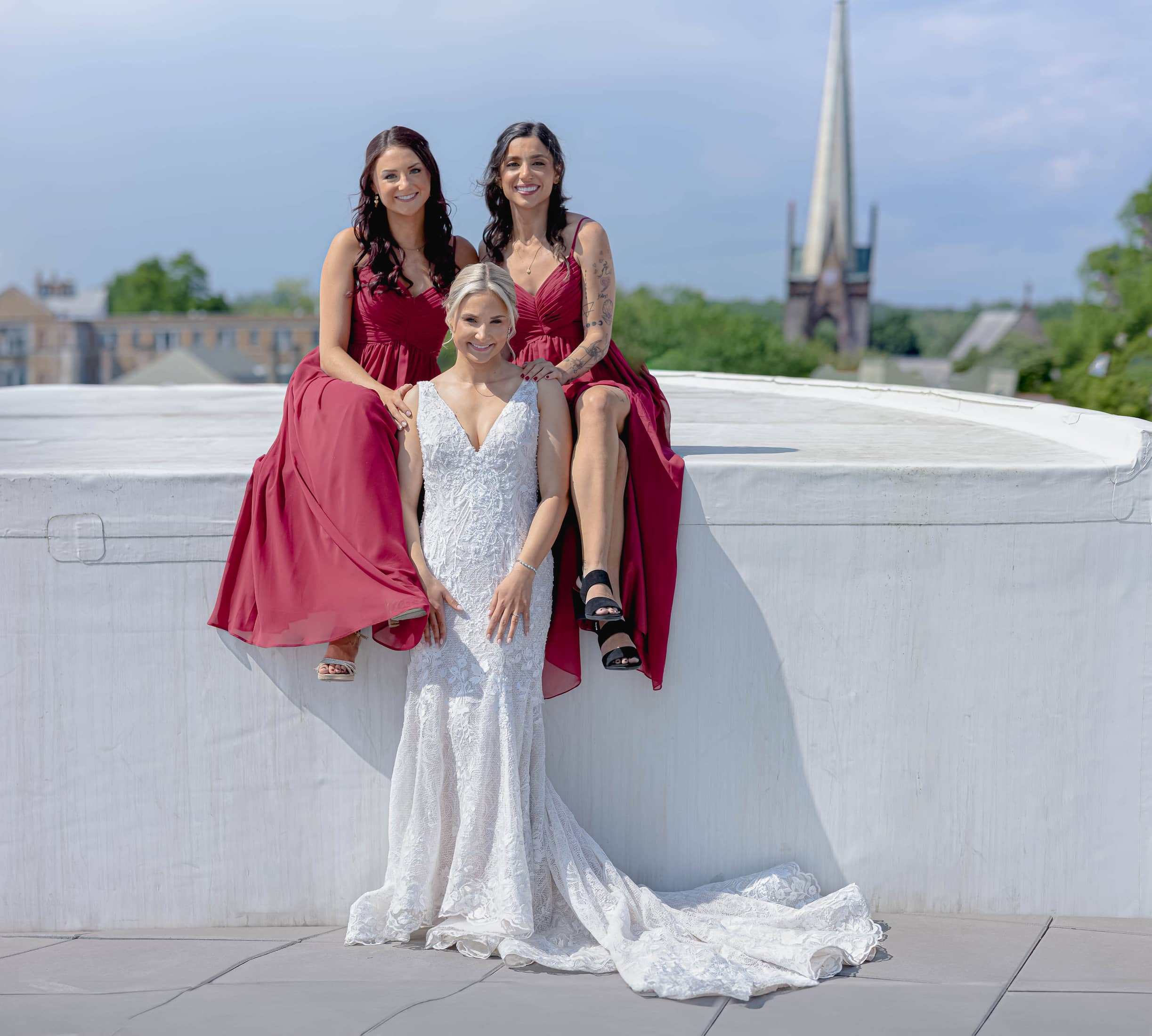 Bride with two Bridesmaids wearing matching red dresses with a fairytale clocktower in the background. Albany brides. Fairytale weddings 