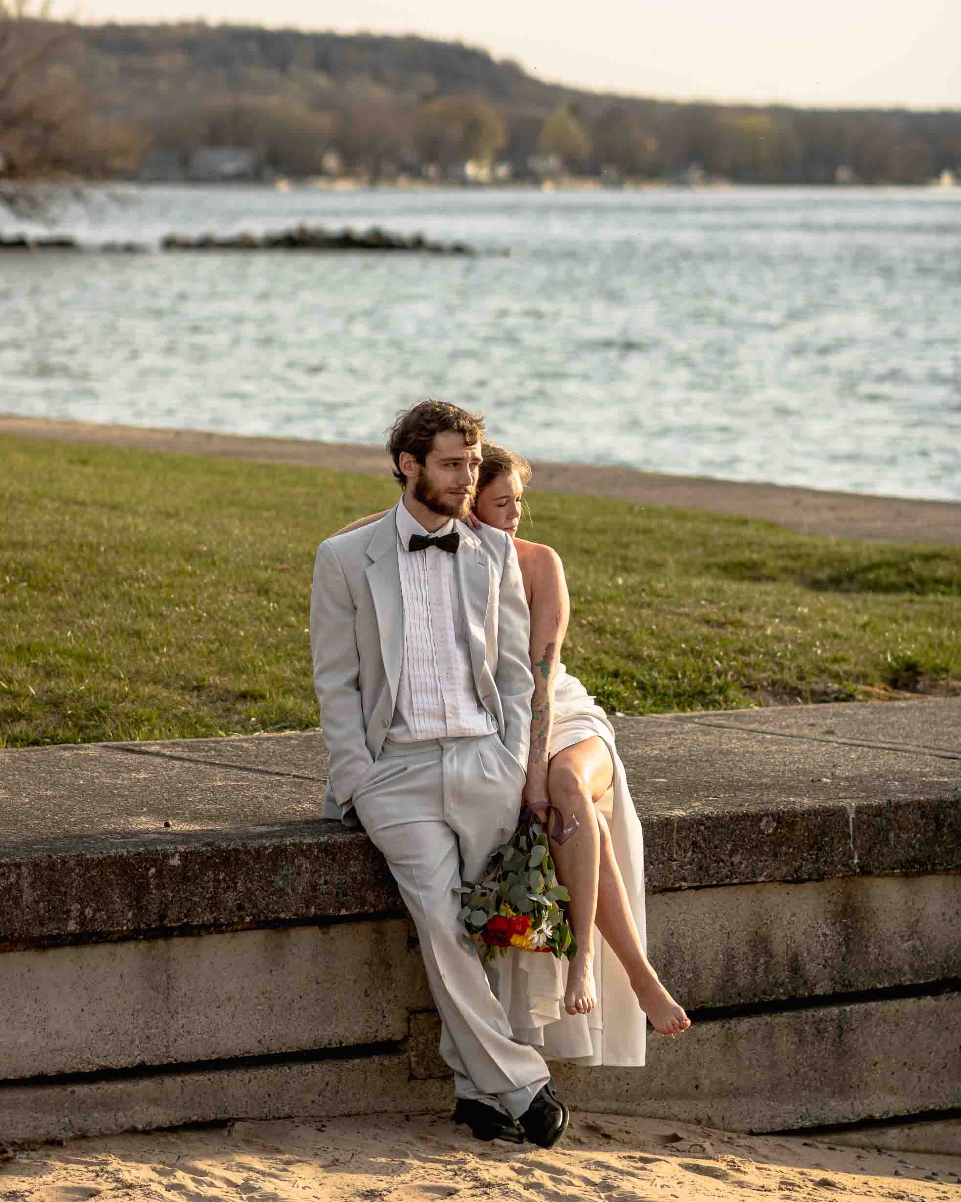 French Riviera wedding. Bride and groom sitting together on a concrete ledge by the beach, sharing a quiet moment.