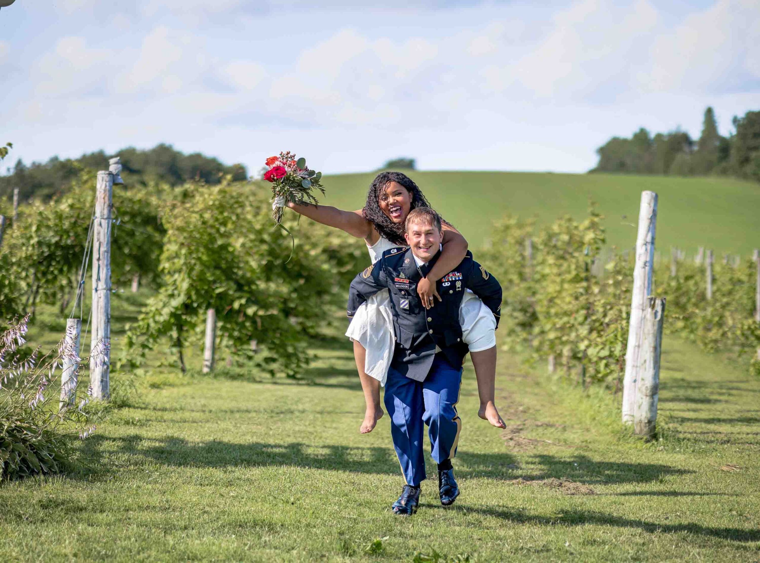 Happy couple piggyback running down a row of grapevines. Winery Wedding.