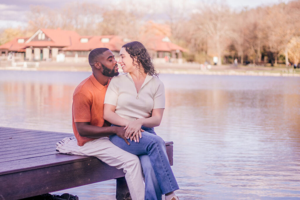 Brianna and Drew sitting closely on a wooden dock over a lake during their autumn engagement photos experience.