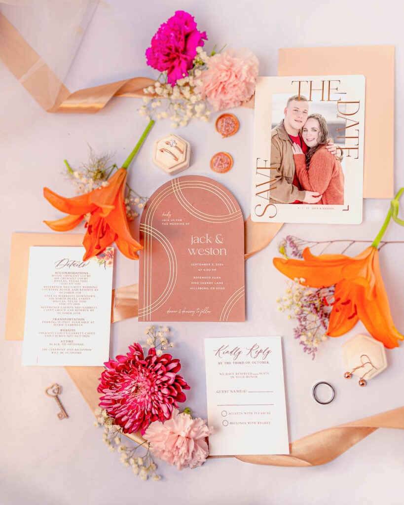 Flat lay of Jack and Weston's wedding invitation suite with vibrant orange tiger lilies and pink flowers.