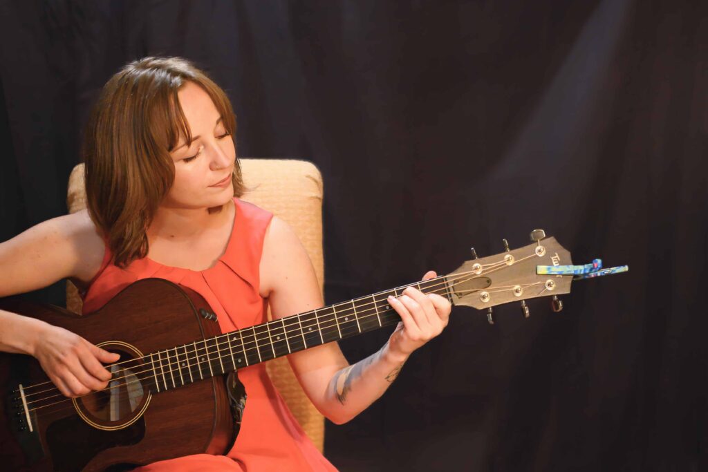  Kylie B in a red dress playing acoustic guitar, providing soulful music at a wedding.