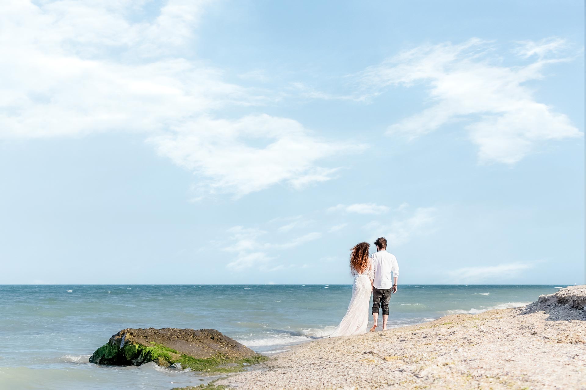 Newlywed couple walking hand in hand along the beach at Lambert's Cove Inn, Martha's Vineyard, with the bride in a flowing gown and the groom in casual wedding attire.