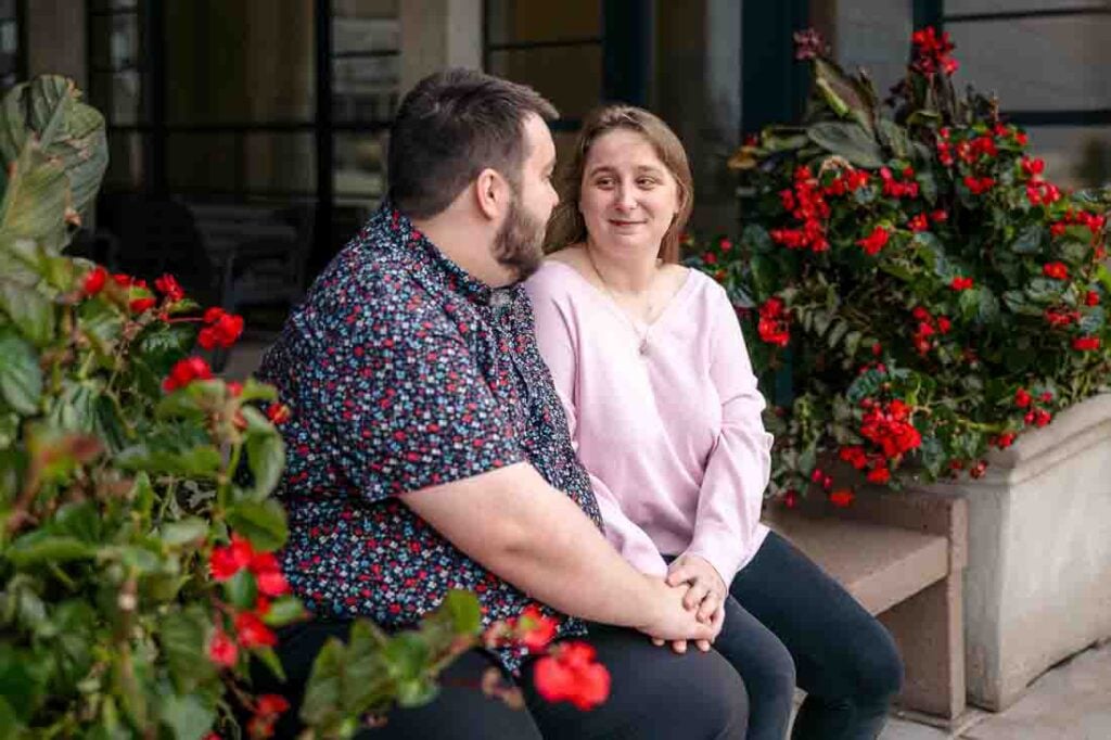 Hanna and Shawn sitting together by a vibrant floral display during their engagement session.