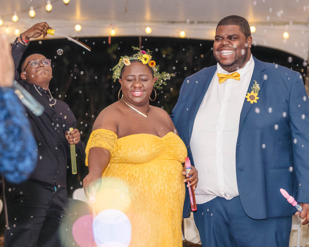 CJ and Danaya joyfully playing with bubble wands at their Knoxville wedding reception under a warmly lit tent.