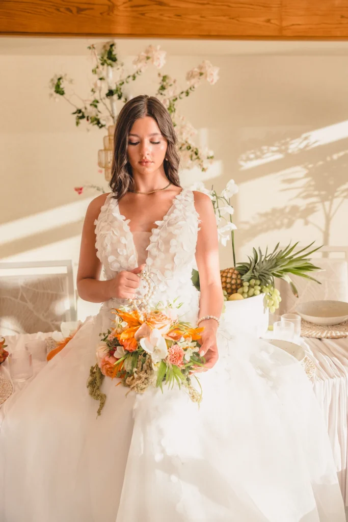Bride in a flowing tulle ball gown holding a tropical bouquet beside the reception table at Kaimana Beach Hotel
