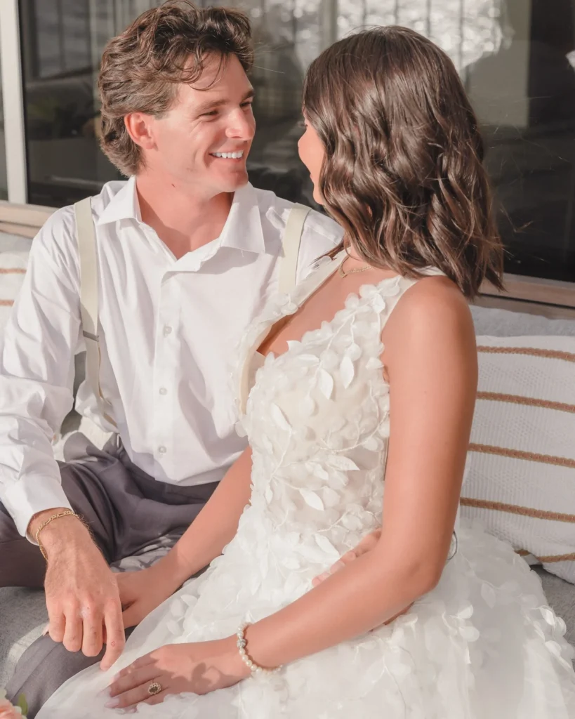Bride and groom laugh together on a lanai lounge sofa at Kaimana Beach Hotel on their wedding day