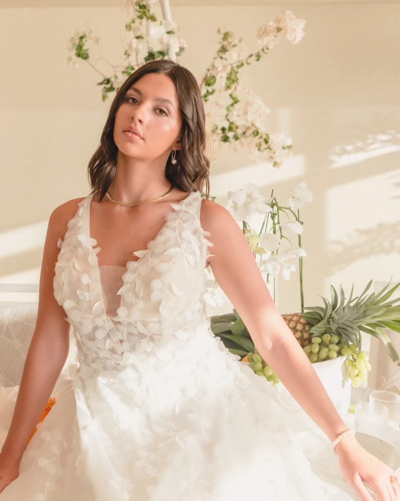 Bride in a plunging V-neck gown with 3D floral appliqués, soft waves and natural glam makeup at Kaimana Beach Hotel