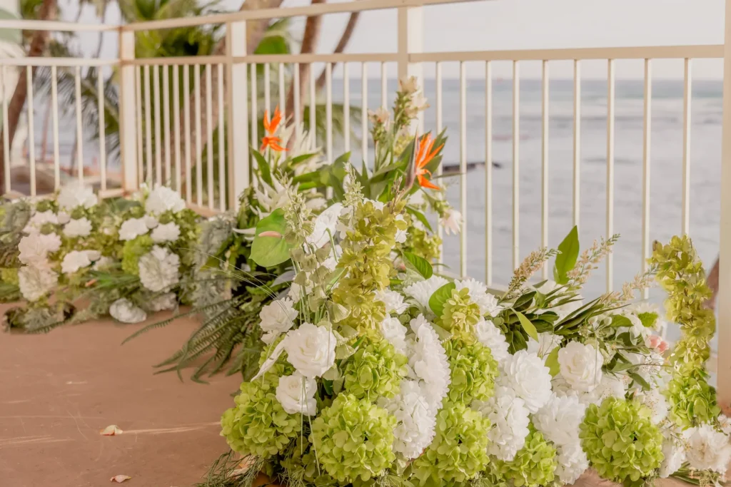 Oceanfront ceremony floral installation with white hydrangeas, green orchids and bird of paradise at Kaimana Beach Hotel