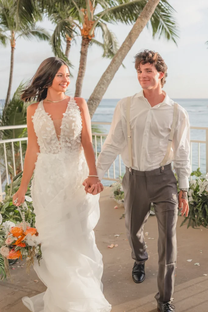 Newlyweds walk hand in hand after their oceanfront ceremony at Kaimana Beach Hotel in Honolulu