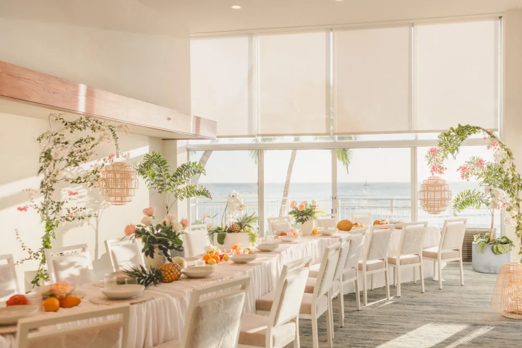 Long reception table with rattan pendant lanterns, orchids and tropical greenery in an oceanview event space at Kaimana Beach Hotel