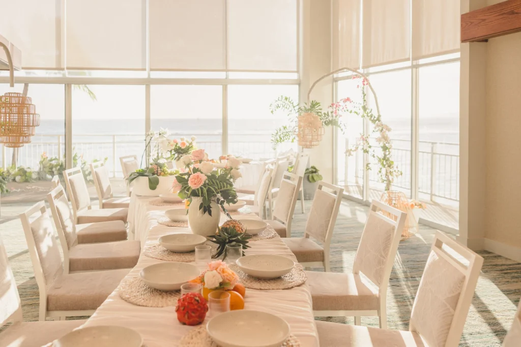 Wedding reception long table with white chairs and tropical floral centerpieces at Kaimana Beach Hotel