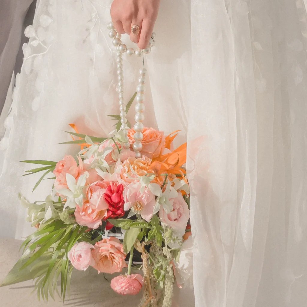 Tropical bridal bouquet of peach roses, lilies and orchids tied with a pearl strand against a lace wedding gown