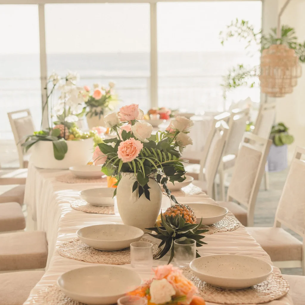 Tropical wedding centerpiece with peach roses, orchids and pineapple on a neutral tablescape overlooking the ocean