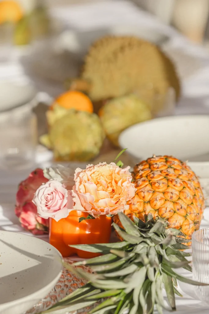 Tropical wedding tablescape detail with pineapple, garden roses and citrus beside a speckled stoneware place setting