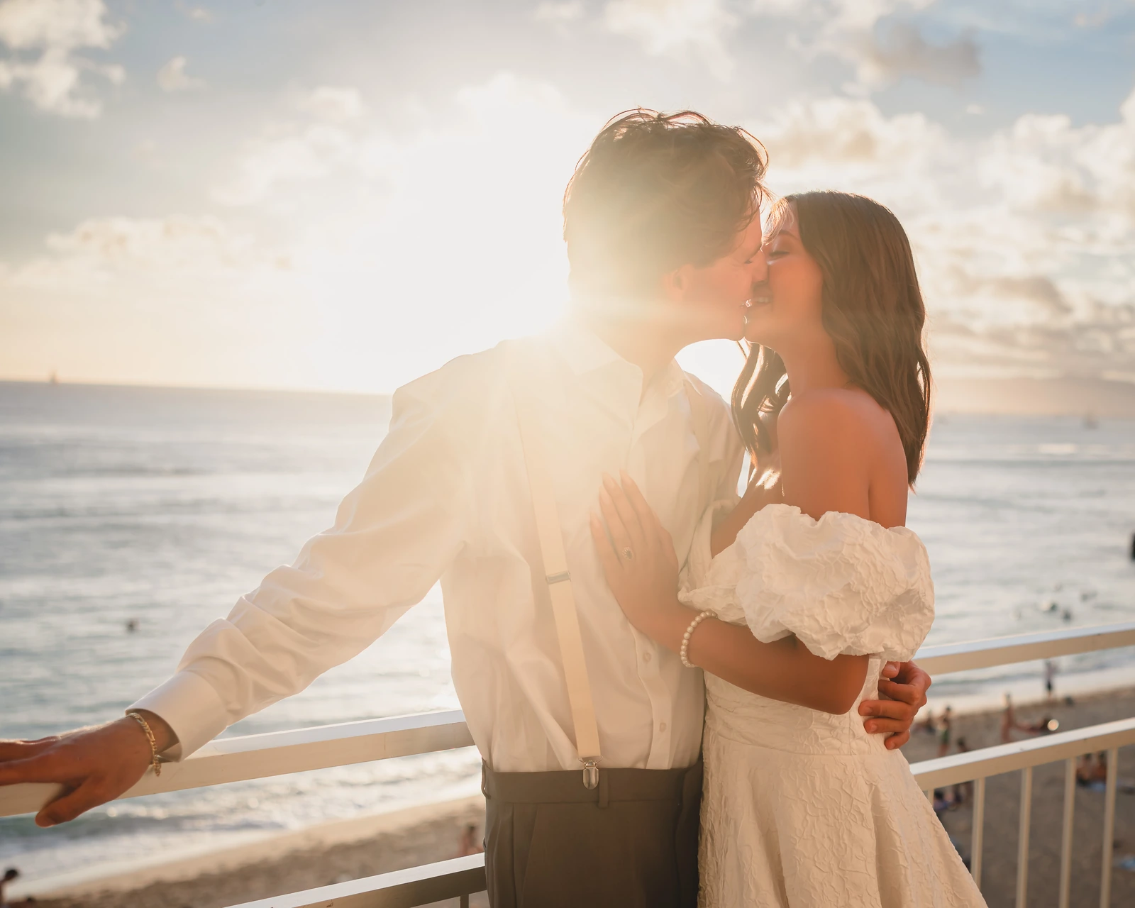 Bride and groom kiss at sunset on an oceanfront lanai at Kaimana Beach Hotel overlooking Waikiki Beach