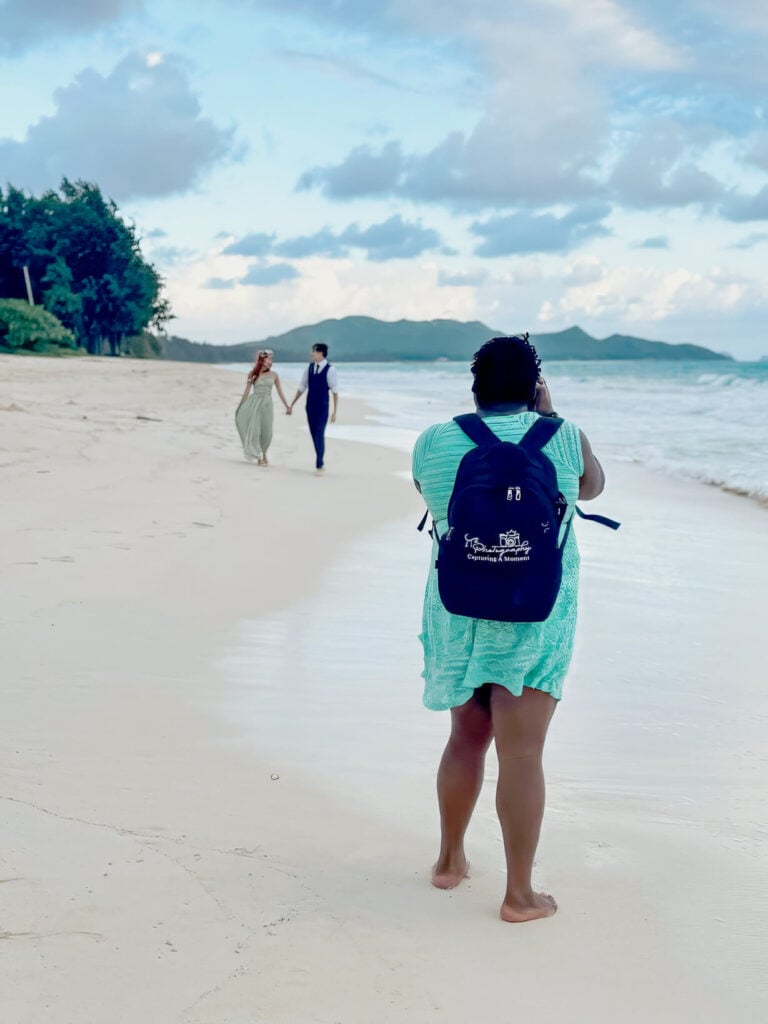 Photographer capturing a couple during a beach engagement session, with a scenic ocean backdrop at Lanikai Beach, Hawaii.