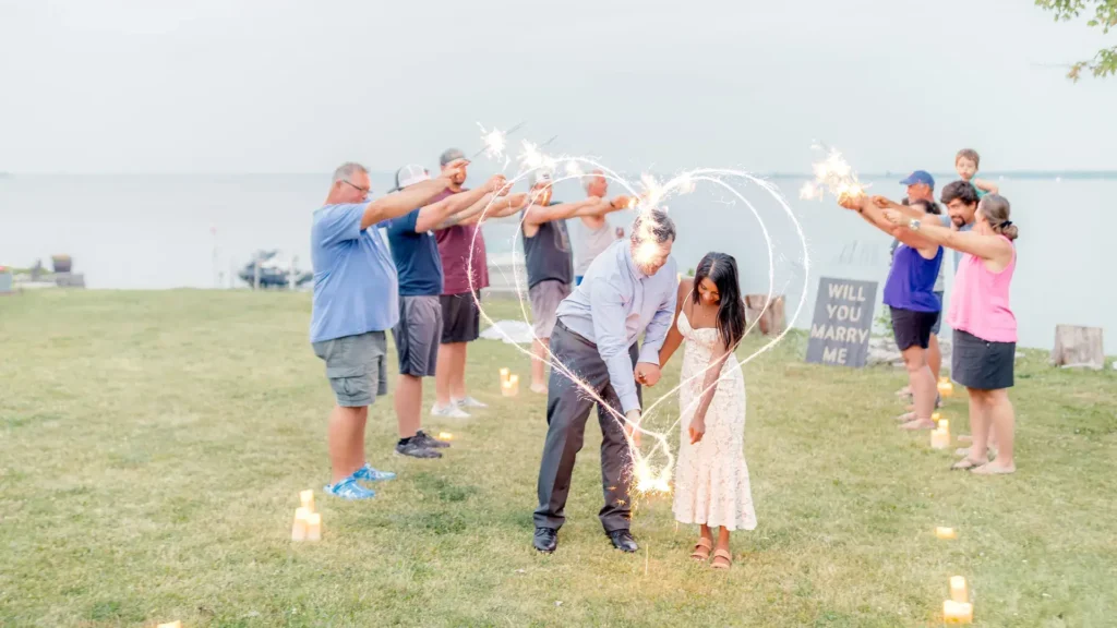 Couple drawing a heart with sparklers while surrounded by family forming a tunnel
