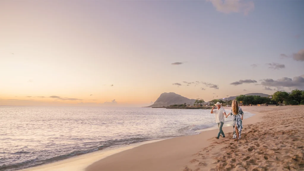 Couple walking hand-in-hand along the beach at sunset in Oahu, Hawaii during an engagement session.
