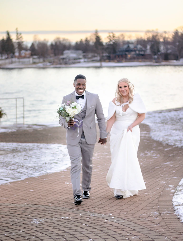 Bride and groom walking hand in hand along a lakeside path at their winter wedding