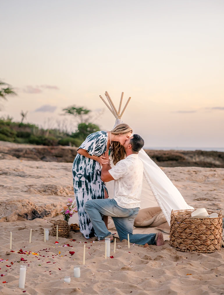 Man proposing on the beach at sunset, couple kissing with romantic candle setup by oahu proposal photography, LT² Photography