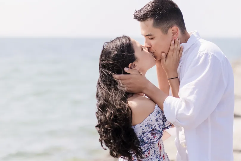 Engagement proposal. Couple kissing beside Lake Ontario after surprise engagement proposal, with eyes closed and hands gently holding each other