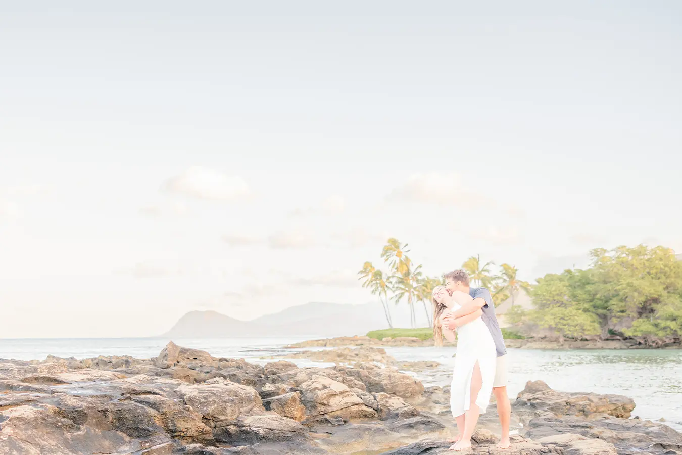 Couple shares a joyful kiss on lava rocks during a sunrise engagement session in Hawaii Title: Romantic Honolulu Sunrise Engagement on the Rocks