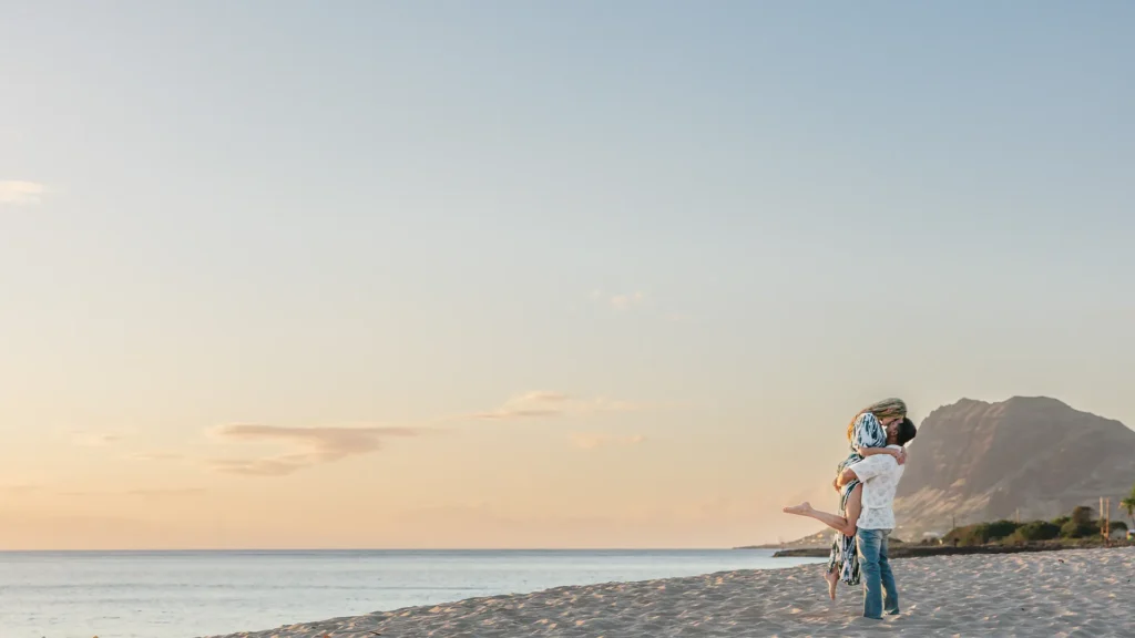 oahu proposal photographer. Man lifts fiancée on a beach at sunset after proposing during a Grand Gesture experience in Oahu