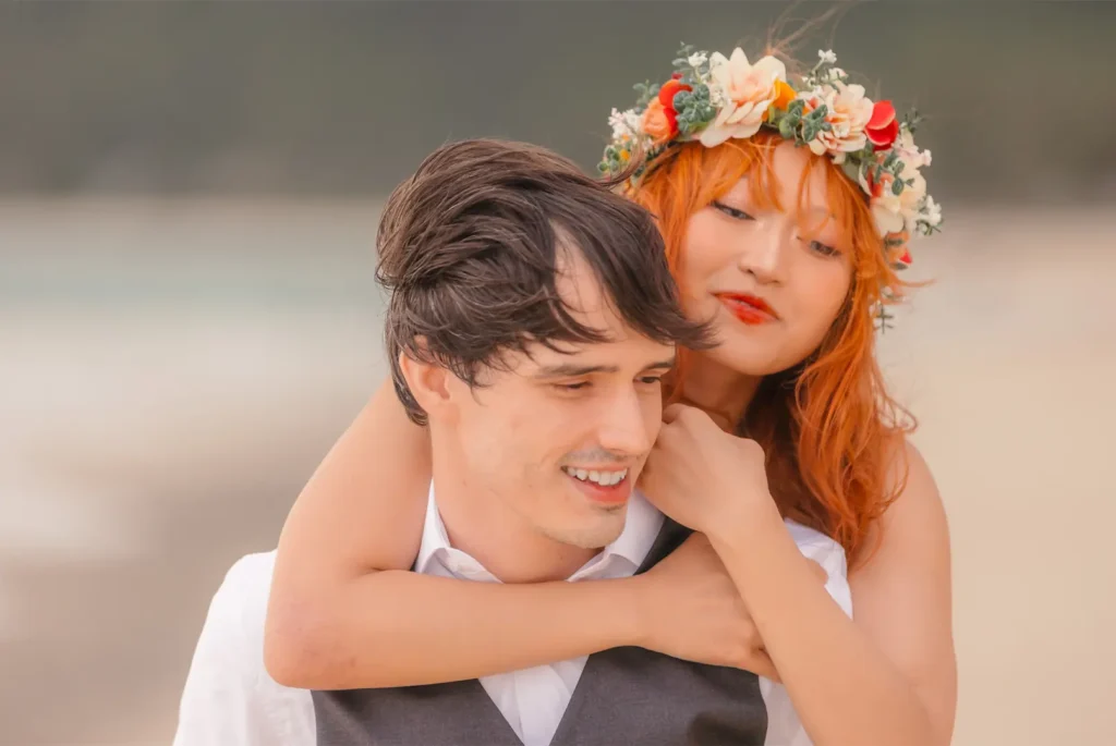 Bride-to-be with a floral crown giving her fiancé a piggyback hug during their beach engagement session in Oahu, Hawaii