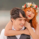 Bride-to-be with a floral crown giving her fiancé a piggyback hug during their beach engagement session in Oahu, Hawaii