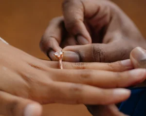 Close-up of a Black couple's engagement moment as a rose gold diamond ring is gently placed on her finger.