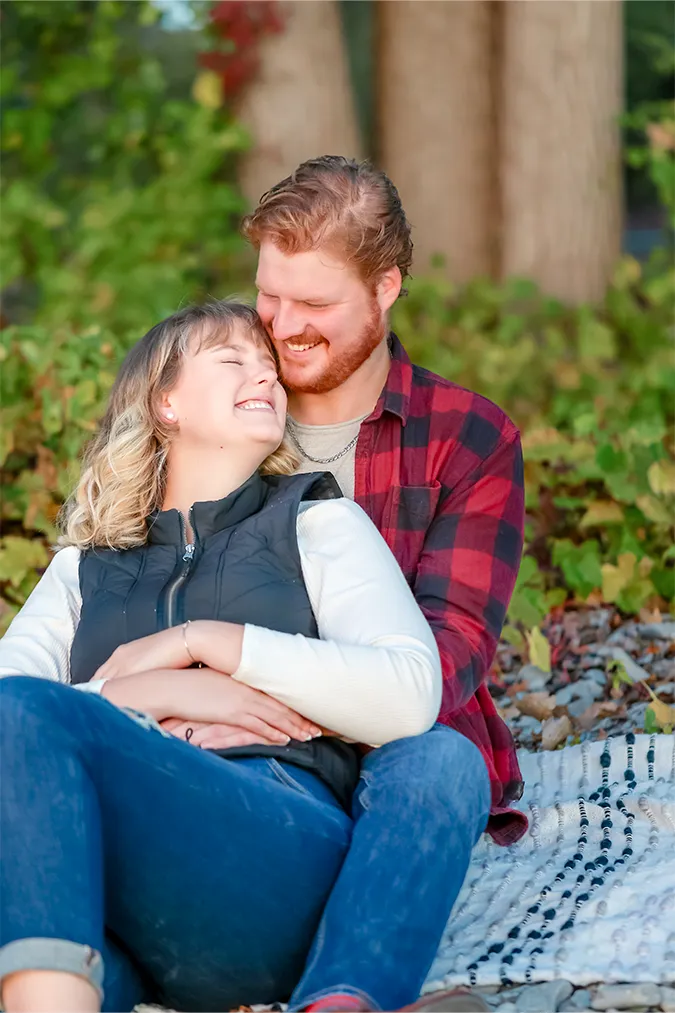 Engaged couple sitting on blanket, smiling at each other