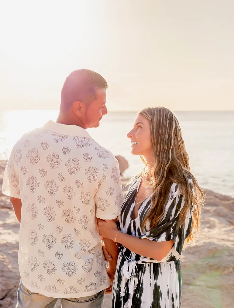 Cheyenne and Loraine smile at each other under the soft golden light of a Hawaii beach sunset, holding hands and laughing together.