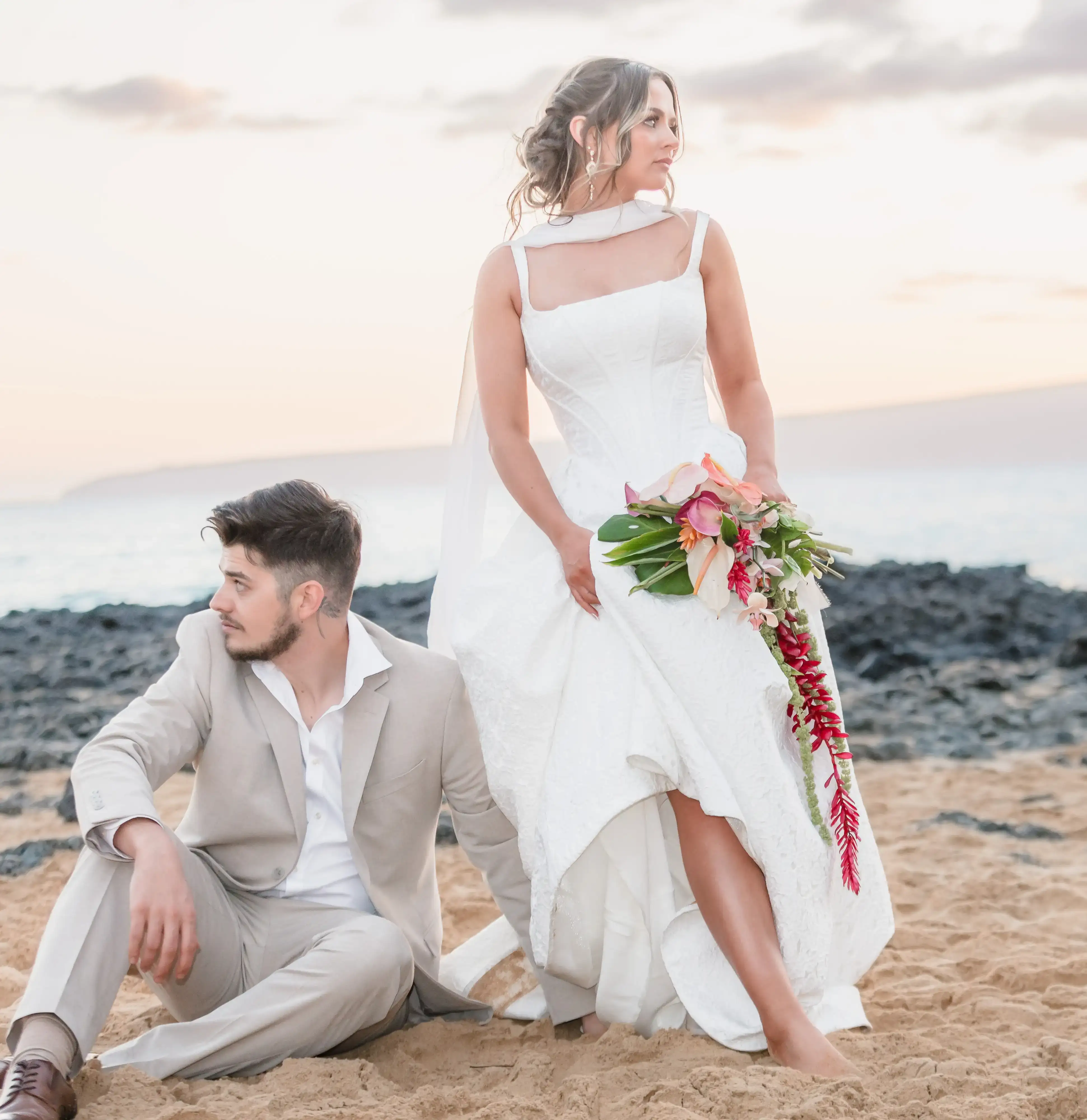 Bride and groom posing on Secret Cover Beach in Maui, Hawaii at sunset with tropical bouquet and ocean views during an elegant Hawaii destination wedding.