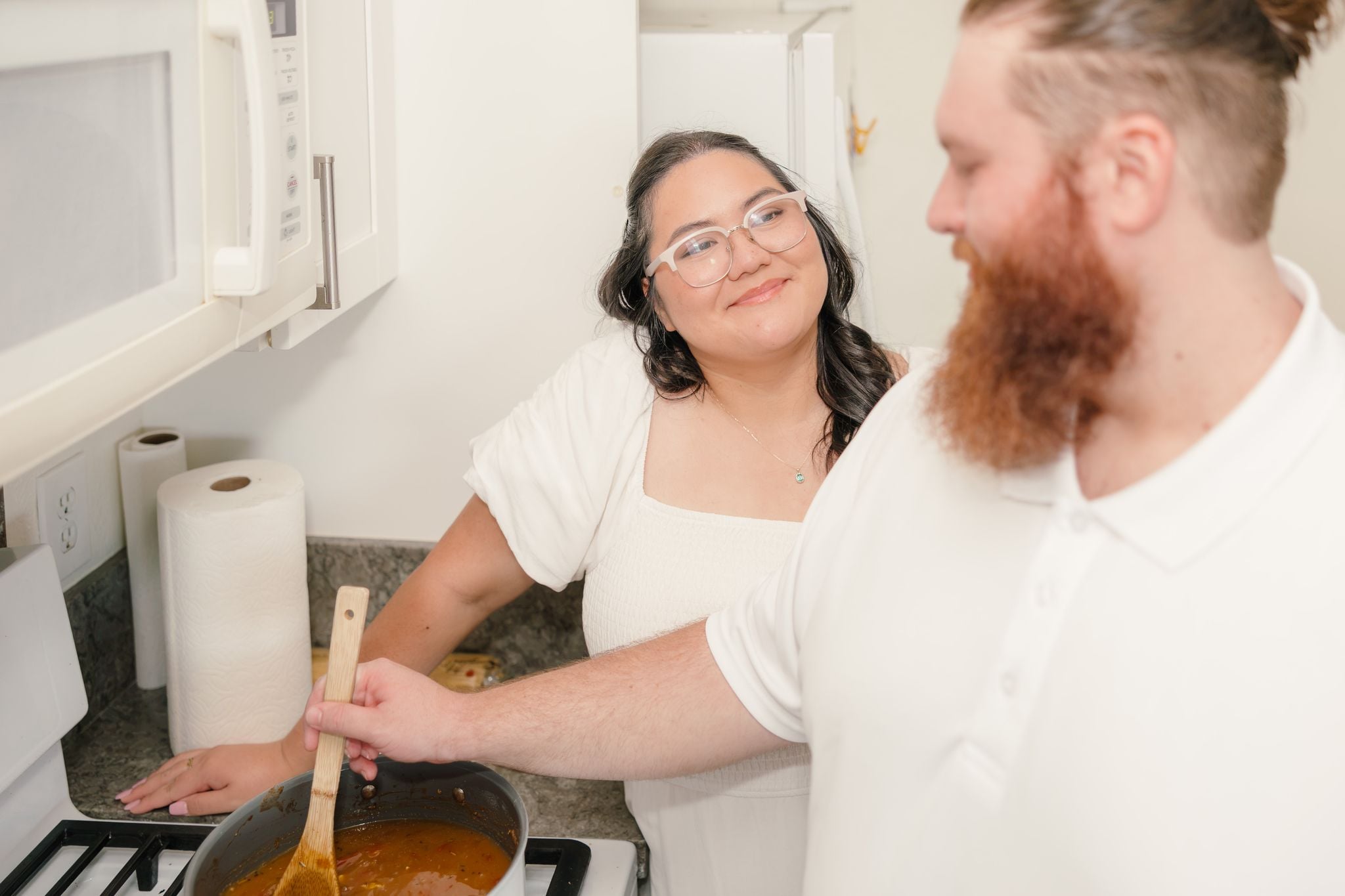 Hope smiles up at Dean as he stirs a pot on the stove in their kitchen.