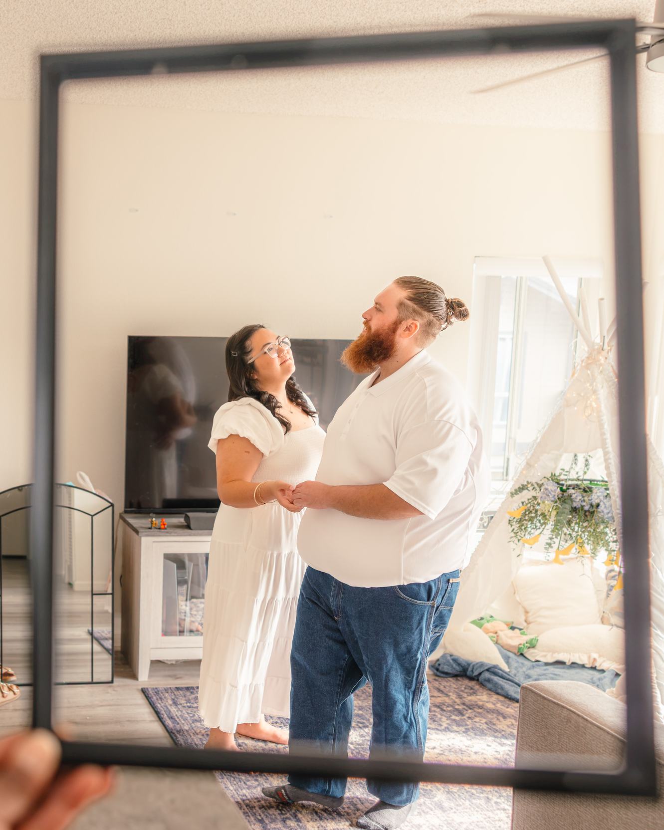 Hope and Dean dance in their living room, seen through an empty picture frame held up to the camera.