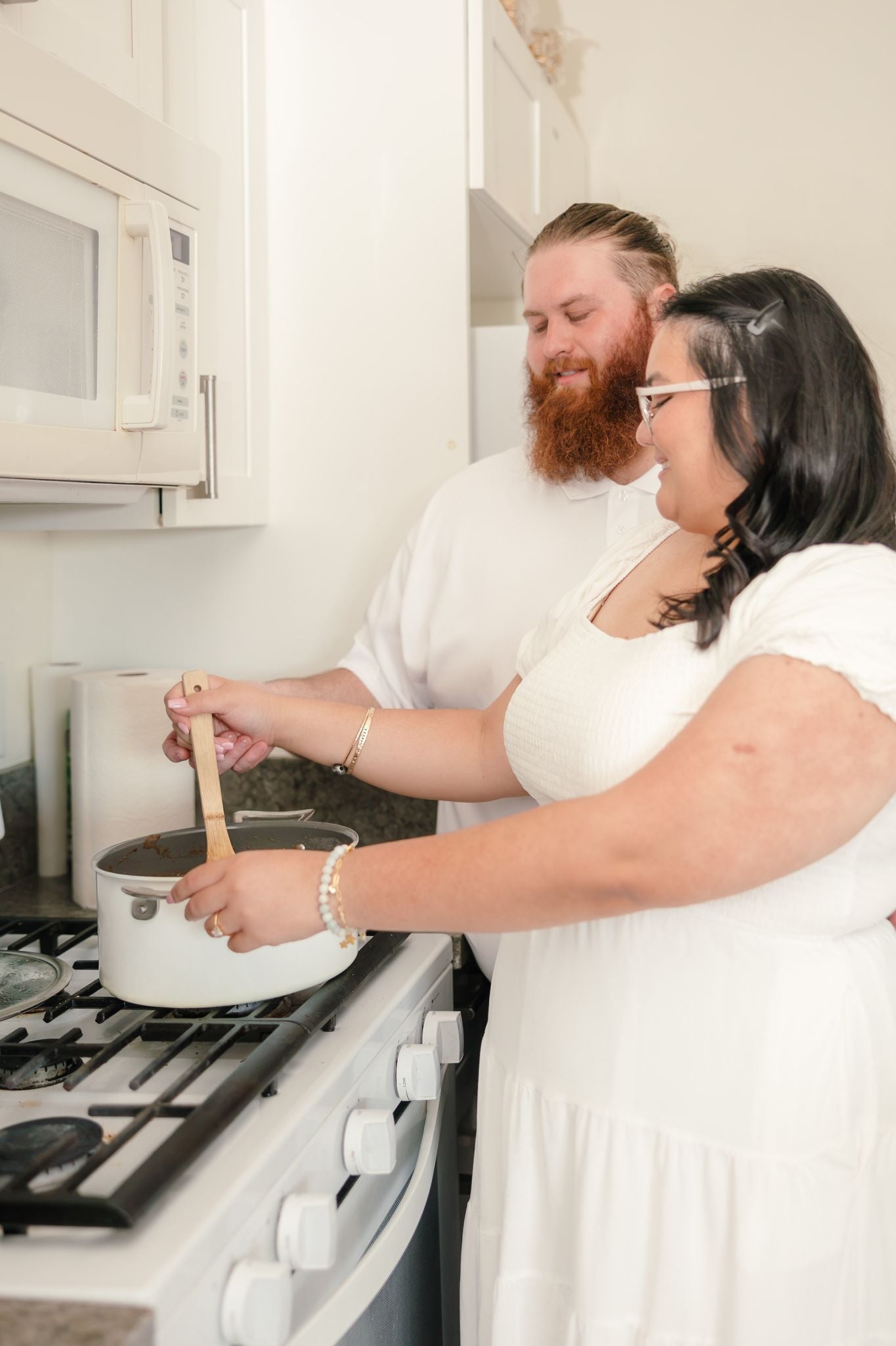 Hope and Dean stir a pot on the stove together, both hands on the wooden spoon, smiling in their kitchen.