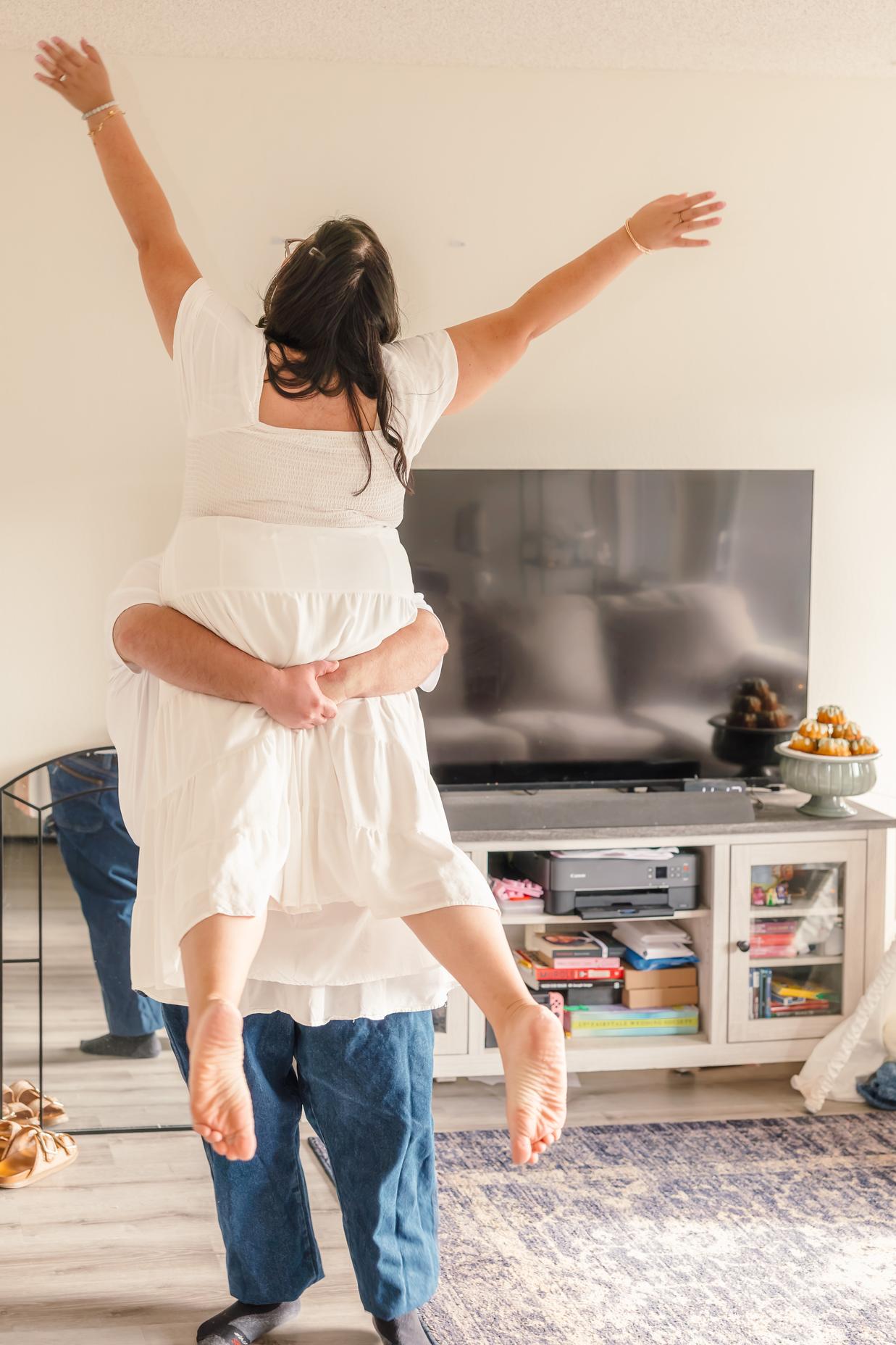 Dean lifts Hope off the ground as she throws her arms up in the air, shown from behind.
