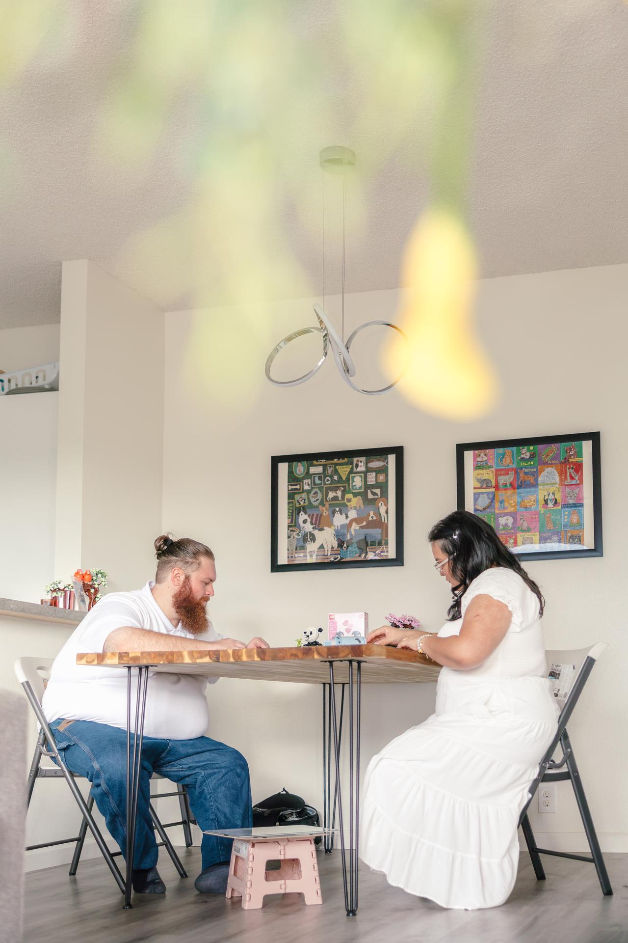 Hope and Dean play a game at their dining table, seen through blurred greenery in the foreground.
