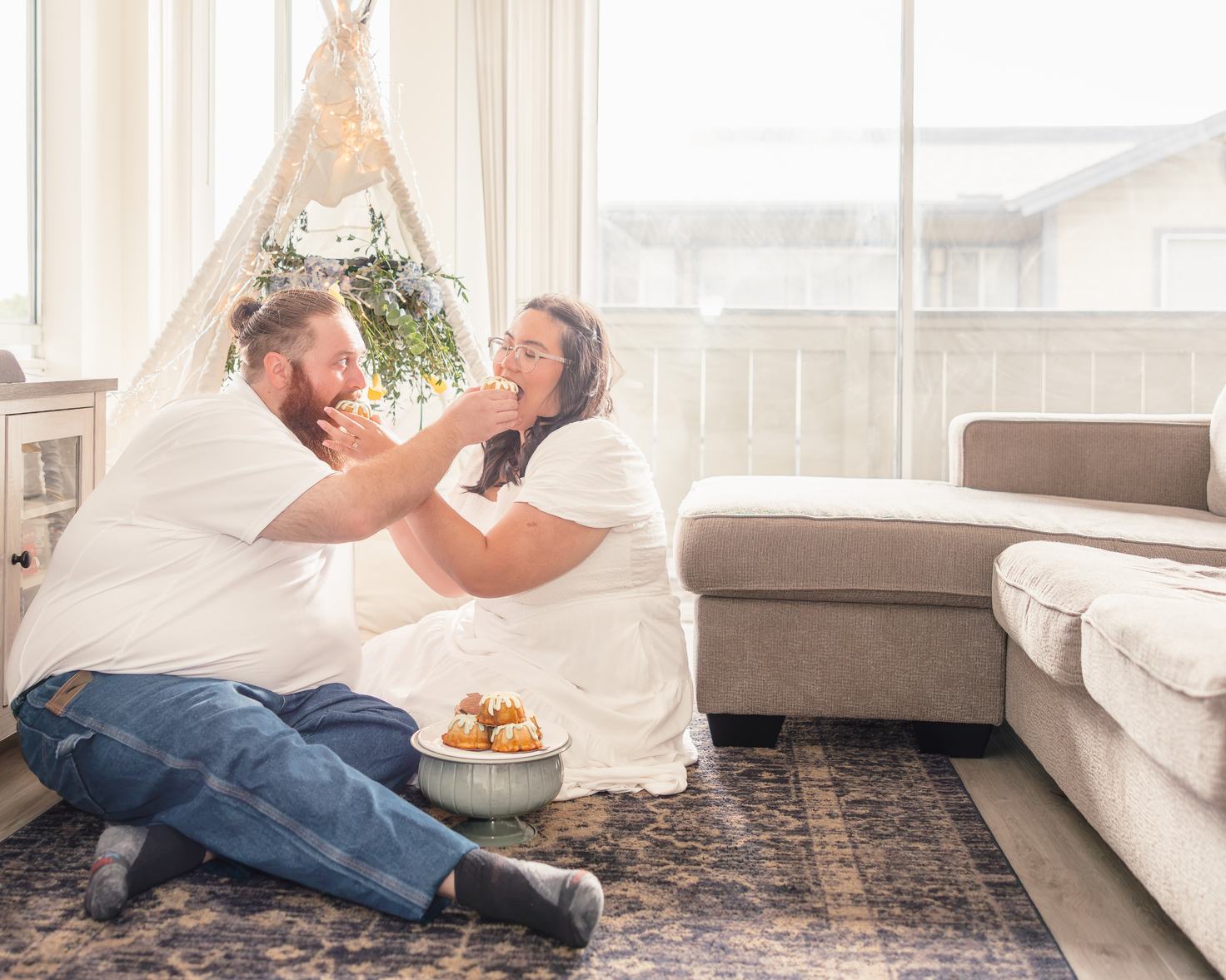Hope and Dean sit on the rug and feed each other mini bundt cakes in front of the teepee.