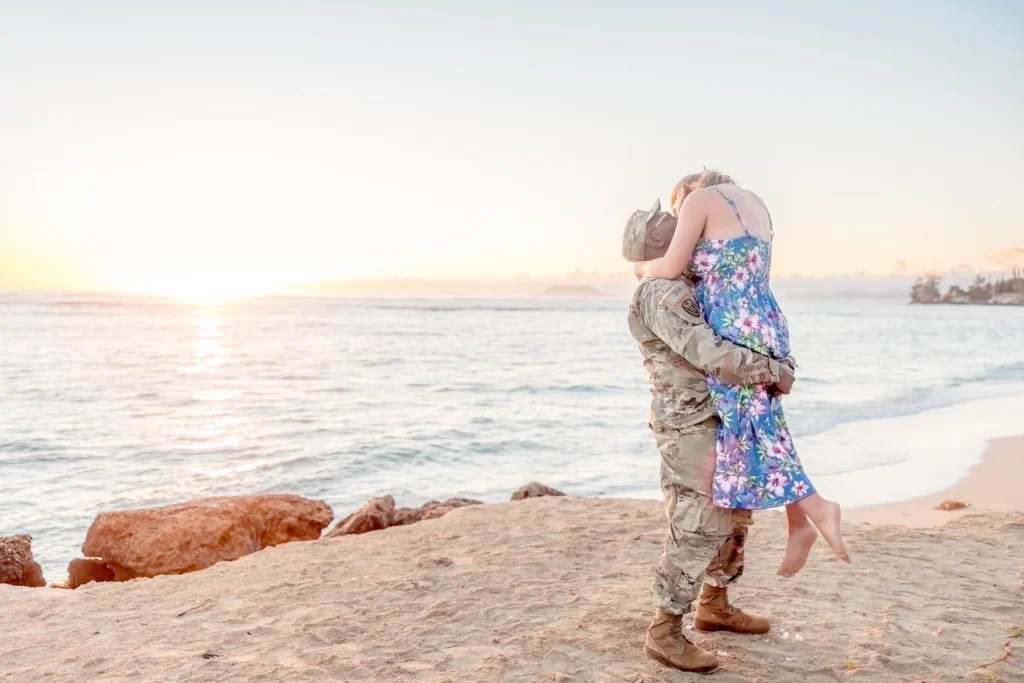 Fiancé lifting his bride-to-be off the sand as the sun rises over the ocean at Kaʻaʻawa Beach, Oahu