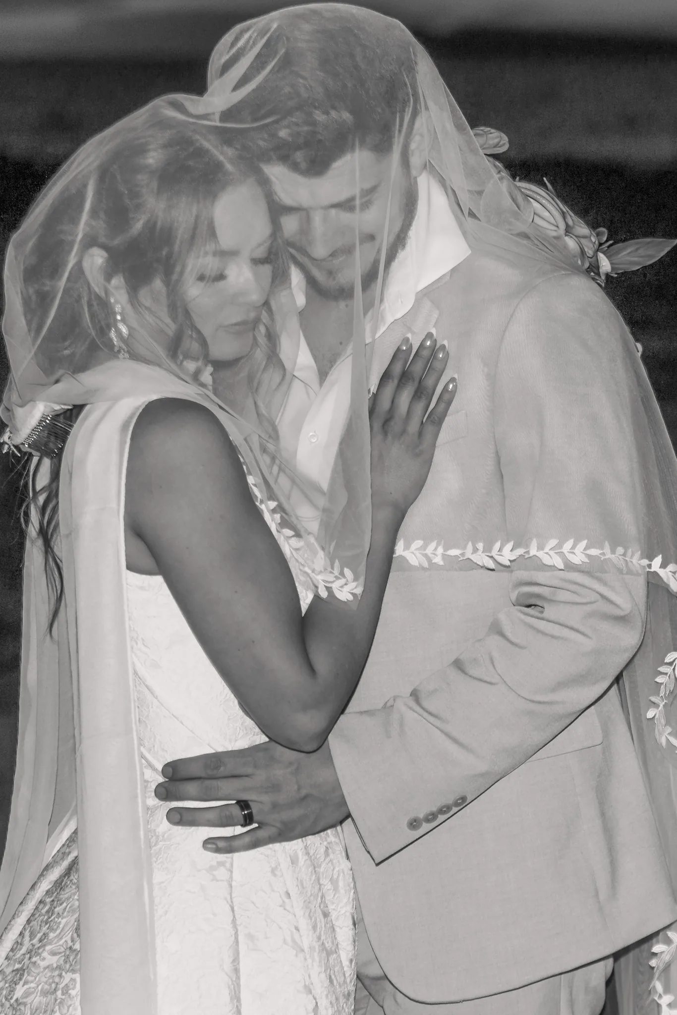 Black and white image of a bride and groom embracing with their eyes closed under her veil