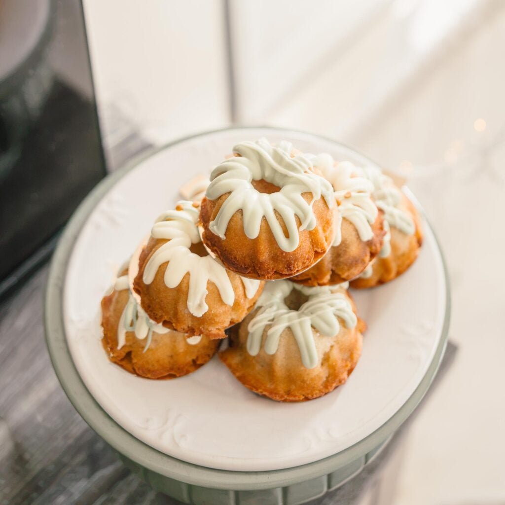 A plate of mini bundt cakes with pale green glaze on a cake stand.
