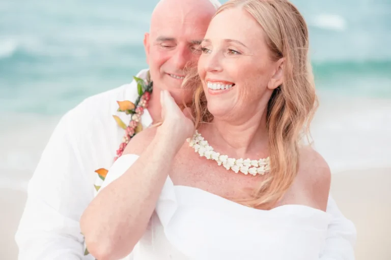 Bride laughing as the groom nuzzles her cheek with the North Shore surf behind them