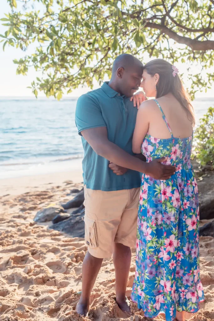 Engaged couple embracing beneath a beachside tree at Kaʻaʻawa on Oahu's windward coast